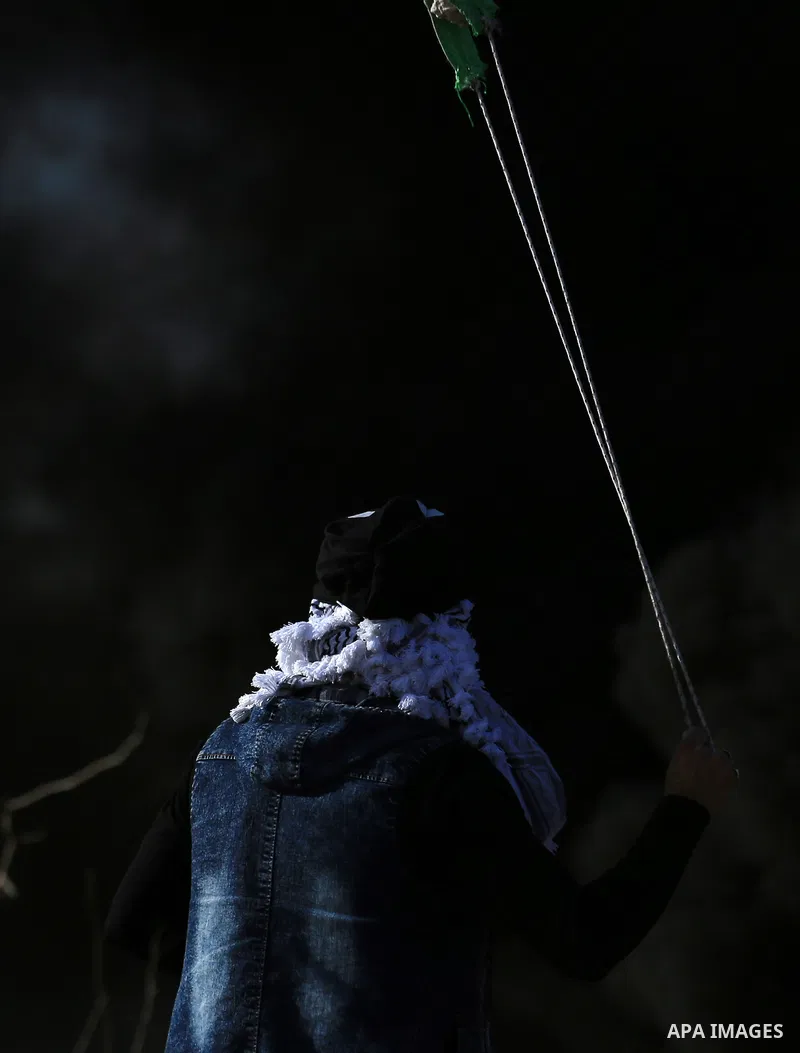 A Palestinian protester uses a slingshot to hurl stones towards Israeli security forces during clashes in the West Bank town of Tulkarem, following a demonstration against US President Donald Trump's decision to recognis...