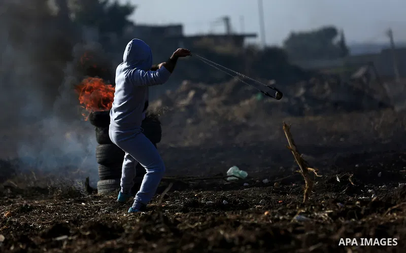 A Palestinian protester uses a slingshot to hurl stones towards Israeli security forces during clashes in the West Bank town of Tulkarem, following a demonstration against US President Donald Trump's decision to recognis...