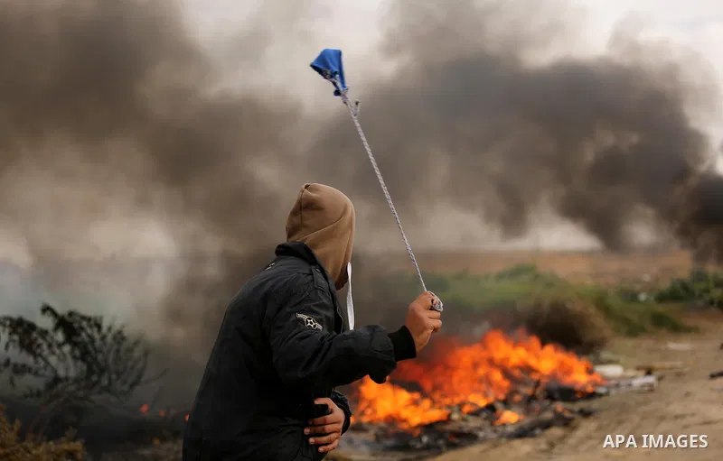 A Palestinian protester uses a slingshot to hurl stones towards Israeli security forces during clashes near the Israel-Gaza border east of the southern Gaza strip city of Khan Yunis on December 12, 2017 with Israeli heav...