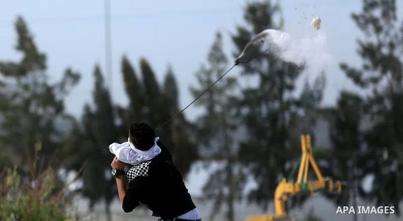 A Palestinian protester uses a slingshot to hurl stones towards Israeli security forces during clashes in the West Bank town of Tulkarem, following a demonstration against US President Donald Trump's decision to recognis...