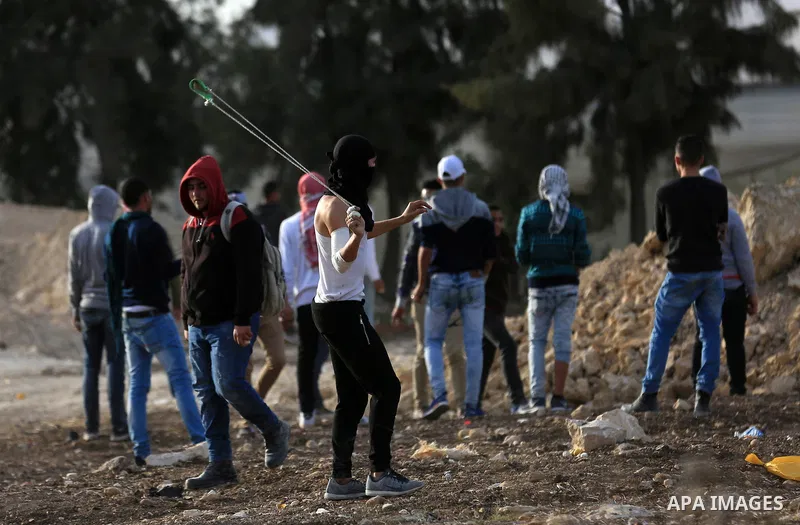 A Palestinian protester uses a slingshot to hurl stones towards Israeli security forces during clashes in the West Bank town of Tulkarem, following a demonstration against US President Donald Trump's decision to recognis...