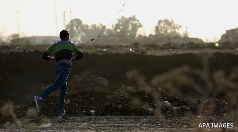 A Palestinian protester uses a slingshot to hurl stones towards Israeli security forces during clashes in the West Bank town of Tulkarem, following a demonstration against US President Donald Trump's decision to recognis...