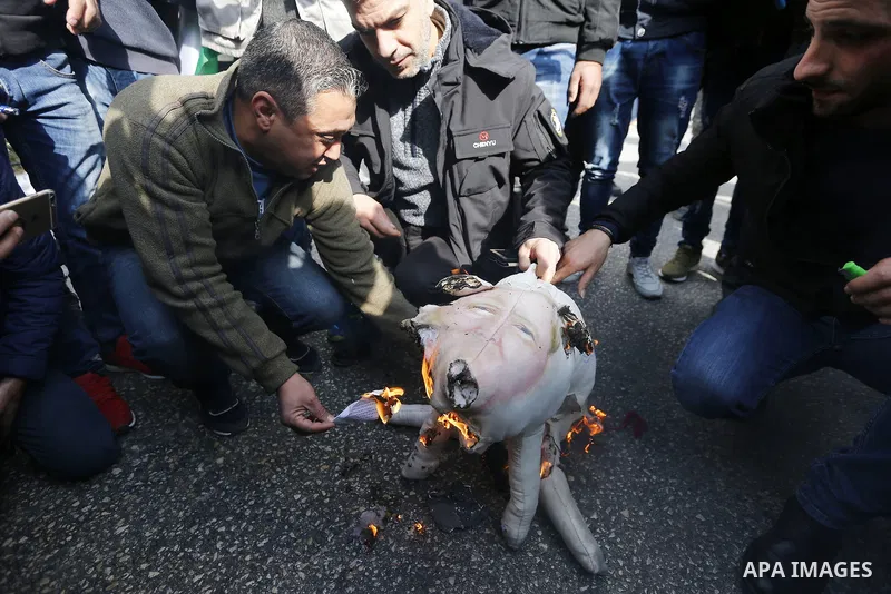 Palestinian protestors burn stuffed pillows in the shape of a pig and bearing an image of Israeli President Benjamin Netanyahu during a demonstration in the West Bank town of Hebron on December 13, 2017. Photo by Wisam H...
