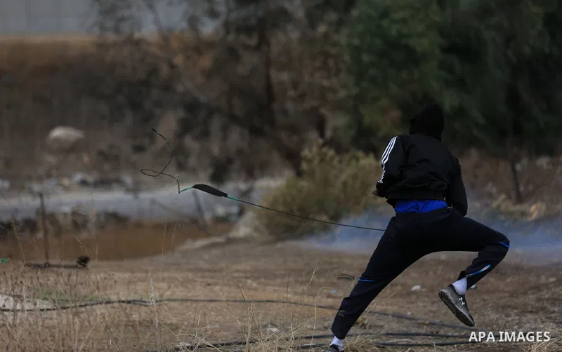 A Palestinian protester uses a slingshot to hurl stones towards Israeli security forces during clashes in the West Bank town of Tulkarem, following a demonstration against US President Donald Trump's decision to recognis...