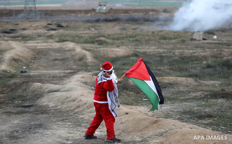 A Palestinian demonstrator dressed as Santa Claus gestures as he holds a Palestinian flag during a protest against U.S. President Donald Trump's decision to recognize Jerusalem as the capital of Israel, near the border w...