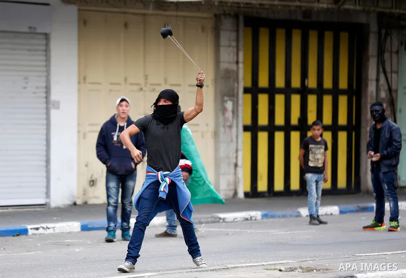A Palestinian protester uses a slingshot to hurl stones towards Israeli security forces during clashes at a protest as Palestinians call for a "Day of Rage" in response to U.S. President Donald Trump's recognition of Jer...