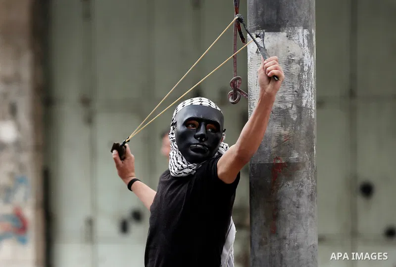 A Palestinian protester uses a slingshot to hurl stones towards Israeli security forces during clashes at a protest as Palestinians call for a "Day of Rage" in response to U.S. President Donald Trump's recognition of Jer...