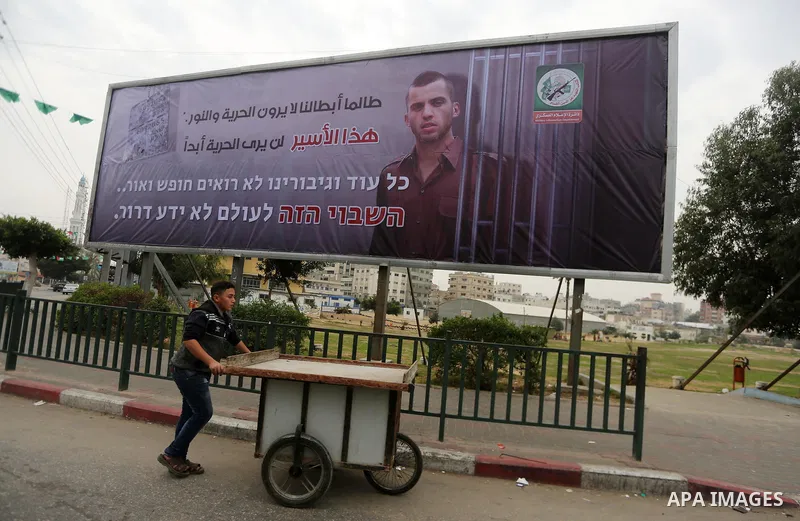 A Palestinian vendor walks past a billboard bearing a portrait of slain Israeli soldier Oron Shaul in Gaza City on December 29, 2017. The writing in Arabic reads: ''As long as our heroes don't see freedom and light: This...