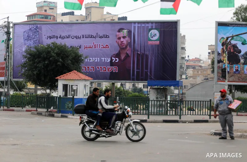 Palestinians walk past a billboard bearing a portrait of slain Israeli soldier Oron Shaul in Gaza City on December 29, 2017. The writing in Arabic reads: ''As long as our heroes don't see freedom and light: This captive...