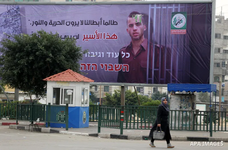 A Palestinian woman walks past a billboard bearing a portrait of slain Israeli soldier Oron Shaul in Gaza City on December 29, 2017. The writing in Arabic reads: ''As long as our heroes don't see freedom and light: This...
