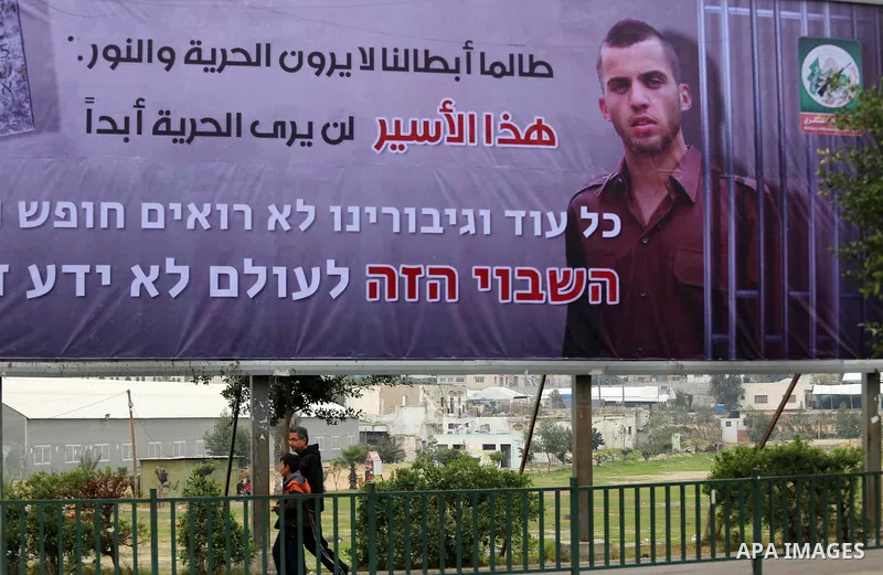 Palestinians walk past a billboard bearing a portrait of slain Israeli soldier Oron Shaul in Gaza City on December 29, 2017. The writing in Arabic reads: ''As long as our heroes don't see freedom and light: This captive...