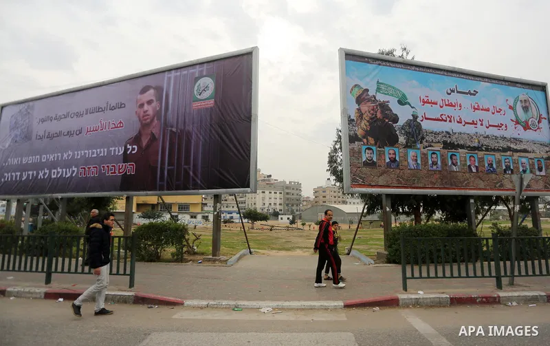 Palestinians walk past a billboard bearing a portrait of slain Israeli soldier Oron Shaul in Gaza City on December 29, 2017. The writing in Arabic reads: ''As long as our heroes don't see freedom and light: This captive...