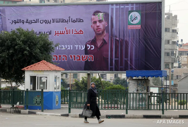 A Palestinian woman walks past a billboard bearing a portrait of slain Israeli soldier Oron Shaul in Gaza City on December 29, 2017. The writing in Arabic reads: ''As long as our heroes don't see freedom and light: This...