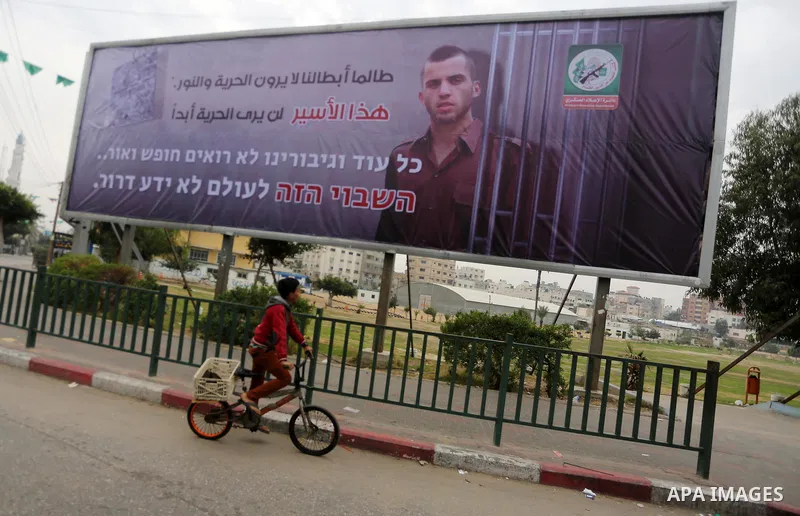 A Palestinian boy rides his bicycle past a billboard bearing a portrait of slain Israeli soldier Oron Shaul in Gaza City on December 29, 2017. The writing in Arabic reads: ''As long as our heroes don't see freedom and li...