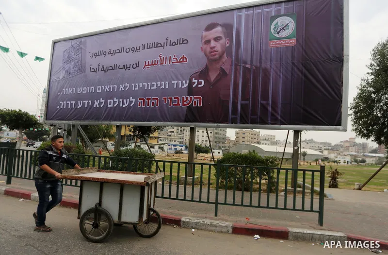 A Palestinian vendor walks past a billboard bearing a portrait of slain Israeli soldier Oron Shaul in Gaza City on December 29, 2017. The writing in Arabic reads: ''As long as our heroes don't see freedom and light: This...