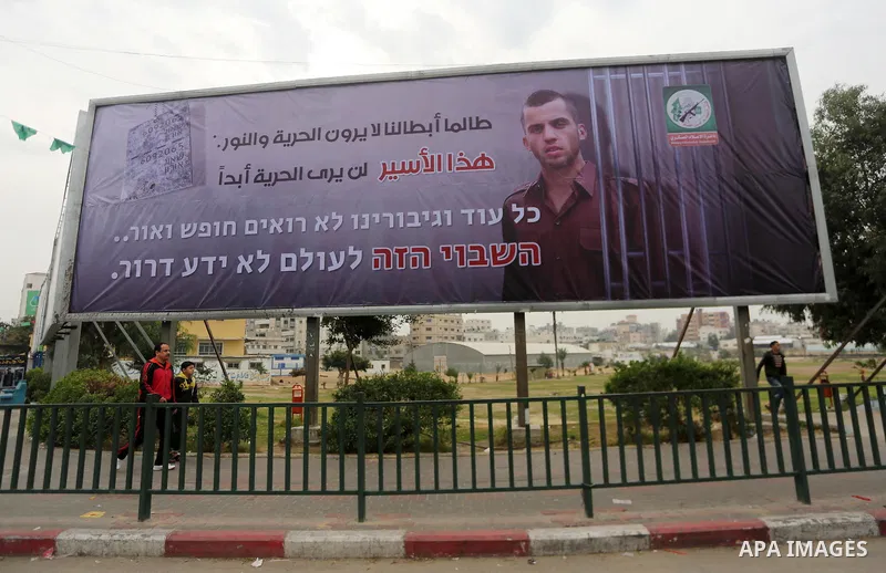 Palestinians walk past a billboard bearing a portrait of slain Israeli soldier Oron Shaul in Gaza City on December 29, 2017. The writing in Arabic reads: ''As long as our heroes don't see freedom and light: This captive...