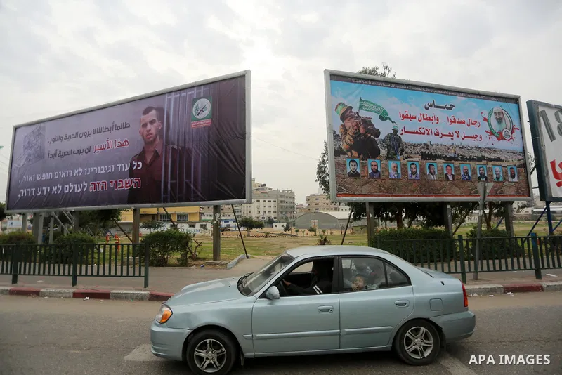 Palestinians walk past a billboard bearing a portrait of slain Israeli soldier Oron Shaul in Gaza City on December 29, 2017. The writing in Arabic reads: ''As long as our heroes don't see freedom and light: This captive...