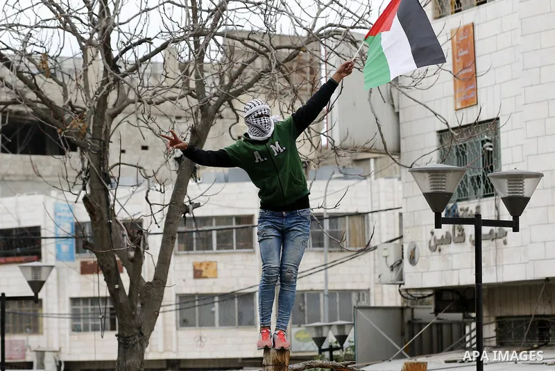 A Palestinian demonstrator waves his country's national flag during clashes with Israeli security forces in the occupied West Bank city of Hebron on December 29, 2017 as protests continue over US President Donald Trump's...