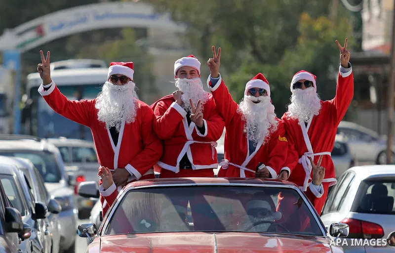 Palestinians dressed as Santa Claus ride a red car to welcome the new year, in the streets of Gaza City, on December 31, 2017. New Year's Eve revellers. Photo by Ashraf Amra