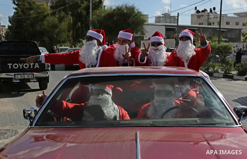Palestinians dressed as Santa Claus ride a red car to welcome the new year, in the streets of Gaza City, on December 31, 2017. New Year's Eve revellers. Photo by Ashraf Amra