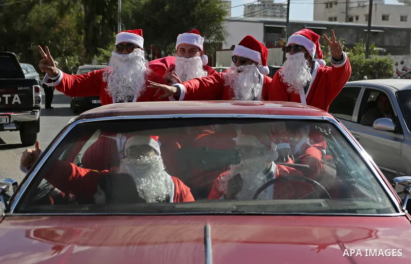 Palestinians dressed as Santa Claus ride a red car to welcome the new year, in the streets of Gaza City, on December 31, 2017. New Year's Eve revellers. Photo by Ashraf Amra