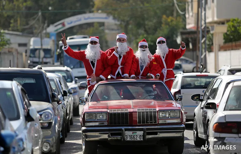 Palestinians dressed as Santa Claus ride a red car to welcome the new year, in the streets of Gaza City, on December 31, 2017. New Year's Eve revellers. Photo by Ashraf Amra