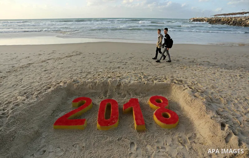 Palestinians man walk past a 2018 sand writing at a beach in Gaza City on December 31, 2017 on the last day of the year. Photo by Ashraf Amra
