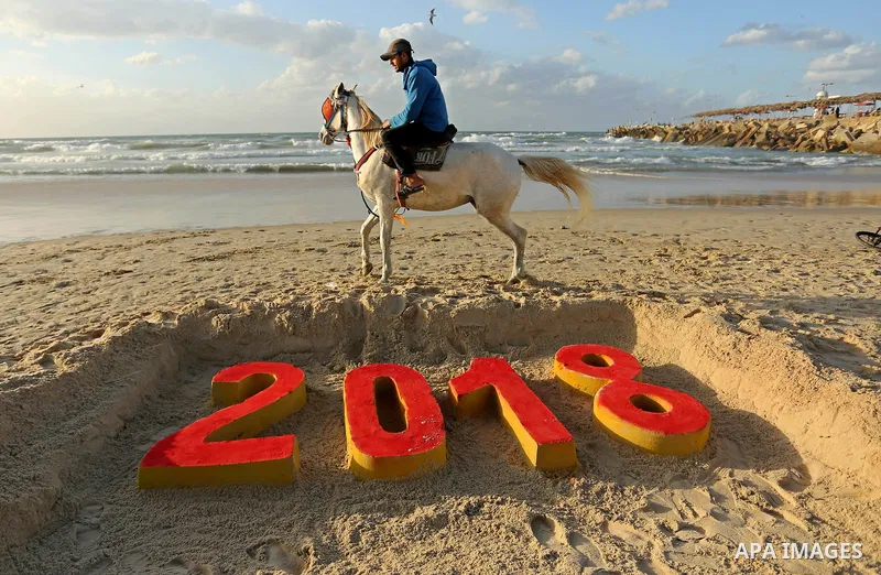 A Palestinian man rides his horse past a 2018 sand writing at a beach in Gaza City on December 31, 2017 on the last day of the year. Photo by Ashraf Amra