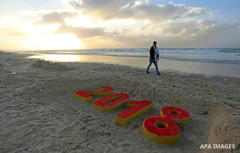 A Palestinian man walks past a 2018 sand writing at a beach in Gaza City on December 31, 2017 on the last day of the year. Photo by Ashraf Amra