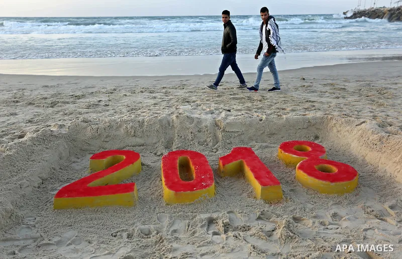 Palestinians man walk past a 2018 sand writing at a beach in Gaza City on December 31, 2017 on the last day of the year. Photo by Ashraf Amra