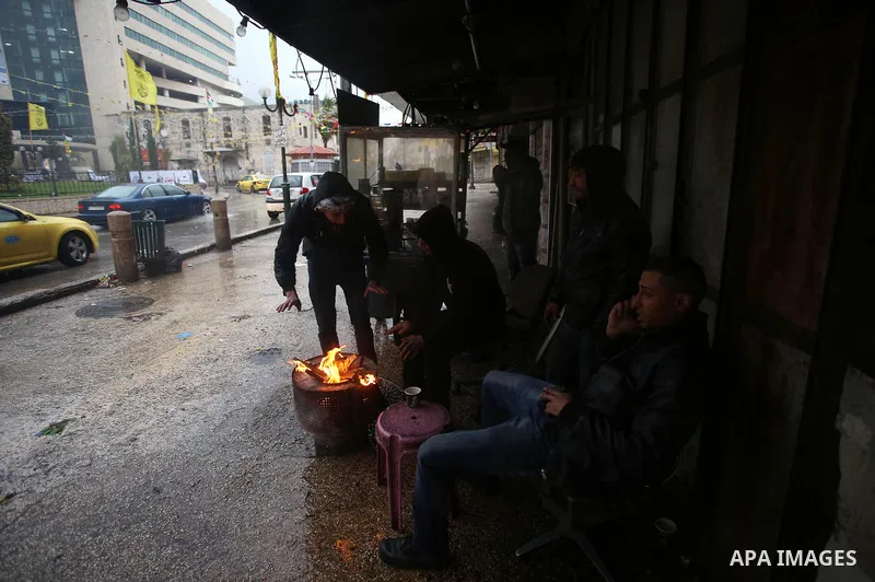 Palestinians warm up themselves in front of a fire at the street as a storm hits the region in the West Bank city of Nablus on January 5, 2018. Palestinian department of Meteorology warned people against gusty winds that...