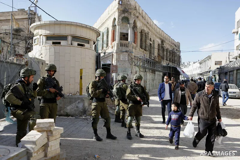 Palestinians walk at a street as Israeli security forces patrol in the Old town in the West Bank city of Hebron on January 14, 2018. Photo by Wisam Hashlamoun