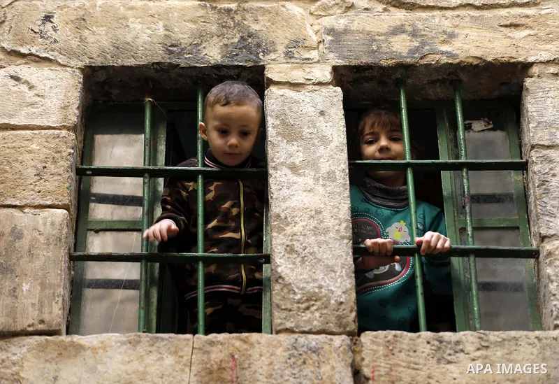 Palestinian children look through a window as Israeli security forces patrol in the Old town in the West Bank city of Hebron on January 14, 2018. Photo by Wisam Hashlamoun