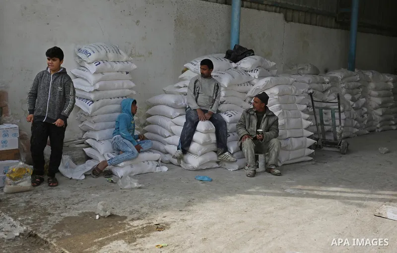 Palestinian men sit on sacks of flour at the United Nations food distribution center in al-Nusirat refugee camp in the Gaza strip on January 17, 2018 after the White House froze tens of millions of dollars in contributio...