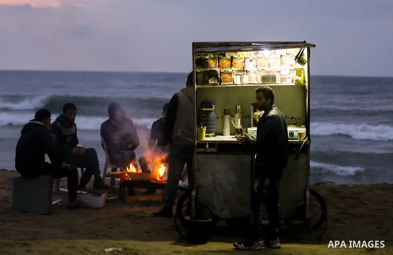 Palestinians warm themselves as a vendor sells hot drinks on a cold day at the sea beach in Gaza City on January 24, 2018. Photo by Yasser Qudih
