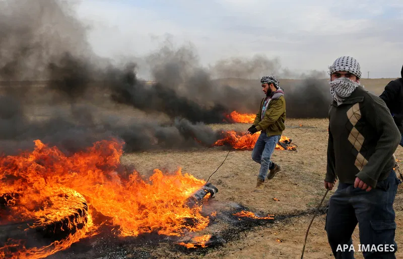A Palestinian protester moves a burning tire during clashes with Israeli security forces, as Palestinians call for 'a day of rage' against US President Donald Trump's decision to recognise Jerusalem as the capital of Isr...
