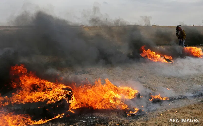 A Palestinian protester moves a burning tire during clashes with Israeli security forces, as Palestinians call for 'a day of rage' against US President Donald Trump's decision to recognise Jerusalem as the capital of Isr...