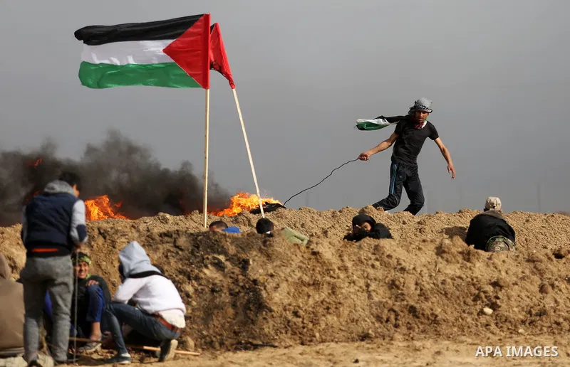 A Palestinian protester moves a burning tire during clashes with Israeli security forces, as Palestinians call for 'a day of rage' against US President Donald Trump's decision to recognise Jerusalem as the capital of Isr...