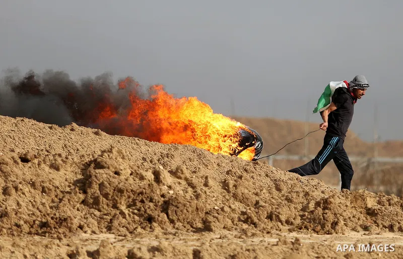 A Palestinian protester moves a burning tire during clashes with Israeli security forces, as Palestinians call for 'a day of rage' against US President Donald Trump's decision to recognise Jerusalem as the capital of Isr...