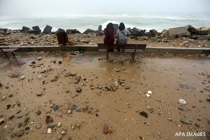 Palestinian women sit in front of the beach on the sea port in Gaza City during a rainy storm on January 27, 2018. Photo by Mohammed Asad