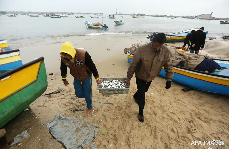 Palestinian fishermen work on their fishing boats on the sea port in Gaza City during a rainy storm on January 27, 2018. Photo by Mohammed Asad