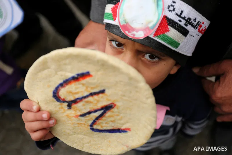 Palestinian children hold bread patties during a protest against aid cuts, outside the United Nations' offices in Khan Yunis in the southern Gaza Strip on January 28, 2018. On January 16, Washington held back $65 million...