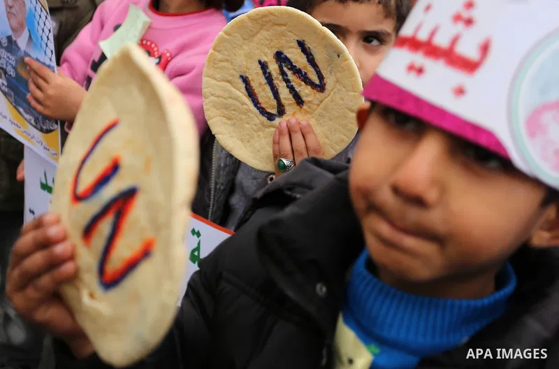 Palestinian children hold bread patties during a protest against aid cuts, outside the United Nations' offices in Khan Yunis in the southern Gaza Strip on January 28, 2018. On January 16, Washington held back $65 million...