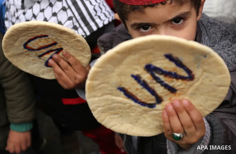 Palestinian children hold bread patties during a protest against aid cuts, outside the United Nations' offices in Khan Yunis in the southern Gaza Strip on January 28, 2018. On January 16, Washington held back $65 million...