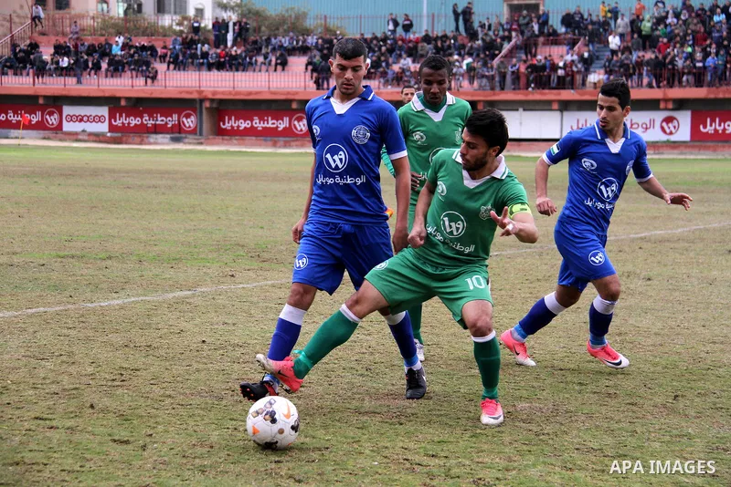 Palestinian players of Khadamat Rafah club (green) and Khadamat al-Shati (blue) compete during a football match at Palestine Stadium in Gaza city on January 28, 2018. Photo by Mahmoud Ajour
