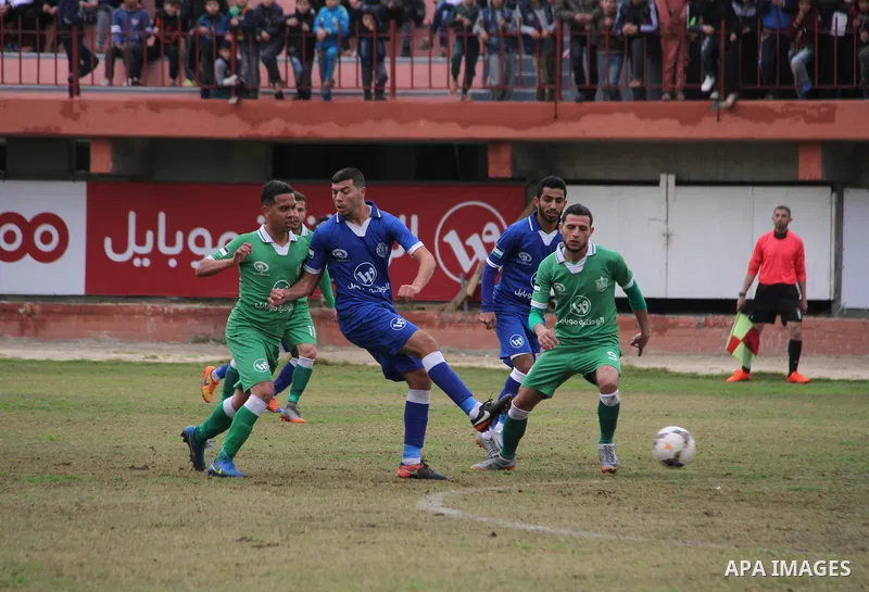 Palestinian players of Khadamat Rafah club (green) and Khadamat al-Shati (blue) compete during a football match at Palestine Stadium in Gaza city on January 28, 2018. Photo by Mahmoud Ajour