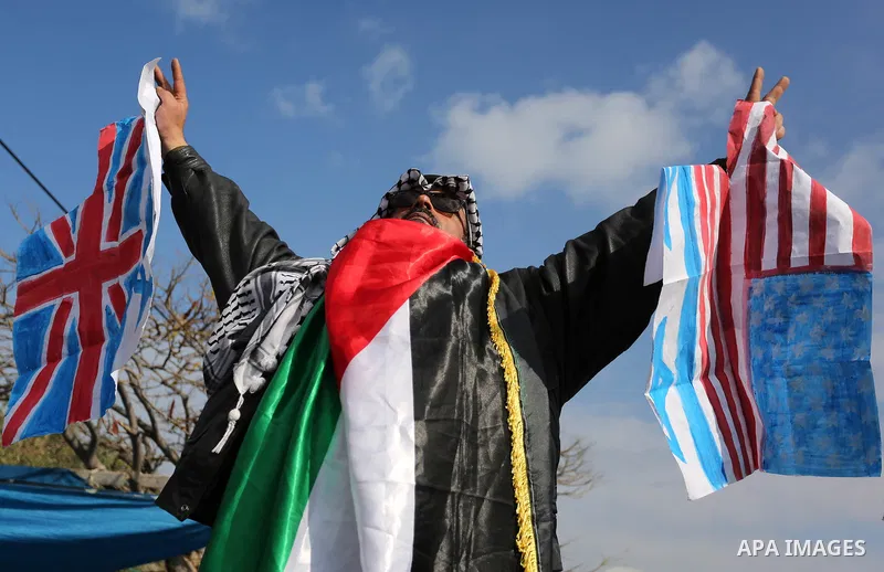 A Palestinian demonstrator gestures as he holds representations of Israeli, British and U.S. flags before burning them during a protest against a U.S. decision to cut aid, in Gaza City January 29, 2018. Photo by Ashraf A...