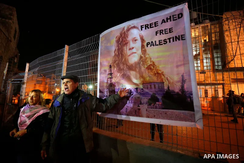 Palestinians stand next to a poster bearing the portrait of Palestinian teen Ahed Tamimi who is detained by Israel, during a symbolic birthday party for her in the West Bank city of Hebron January 30, 2018. Photo by Wisa...