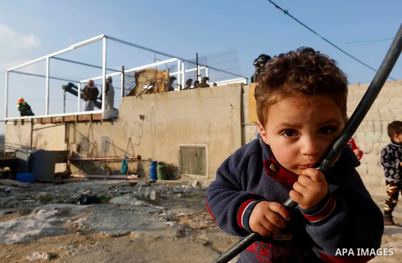 A Palestinian boy poses as Israeli workers guarded by Israeli soldiers dismantle his family structure in the West Bank village of Yatta, near Hebron January 31, 2018. Photo by Wisam Hashlamoun