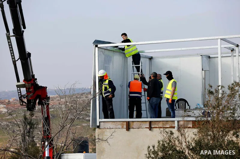 Israeli workers guarded by Israeli soldiers dismantle a Palestinian structure in the West Bank village of Yatta, near Hebron January 31, 2018. Photo by Wisam Hashlamoun